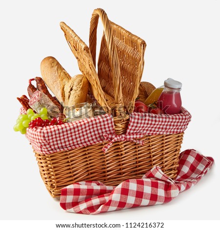 Summer picnic basket filled with food with fresh fruit and juice, spicy salami, baguettes, tomatoes and herb spread isolated on white on a rustic checked tablecloth