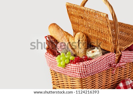 Fresh fruit, bread and cheese in an open wicker picnic basket isolated on white with copy space ready for a summer outdoor lunch