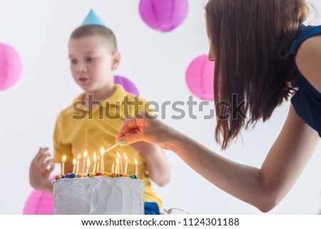 Mother lights candles on the cake and children blow candles