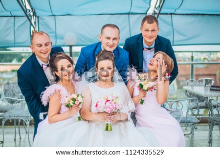 Newlyweds with groomsmen and bridesmaids having fun outdoors. Bride and groom with friends make crazy moments before wedding ceremony.