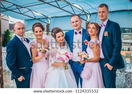 Newlyweds with groomsmen and bridesmaids having fun outdoors. Bride and groom with friends make crazy moments before wedding ceremony.