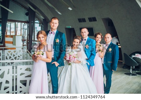 Cheerful and fun groom with bride, bridesmaids with groomsmen posing in hotel reception near large windows. Wedding moment of newlyweds. Bridal day.