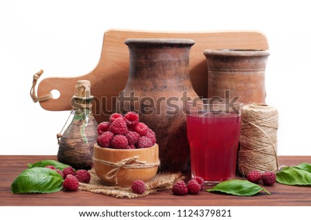 Old dishes, raspberries in a wooden bowl, and a glass of compote on a brown wooden board. White background. Rustic Style