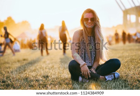 Young beautiful girl during sunset at summer holi festival sitting on grass