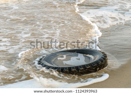 Old black rubber tire left on beach, environment pollution concept, selective focus, color toned picture. Discarded old tyre in blue water on beach. Pollutions and garbages in sea and on beach