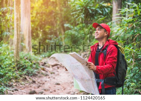 Young asian traveller man searching right direction on map in the forest. Image of lifestyle camping,travel,hiking or recreation concept with copy space.
