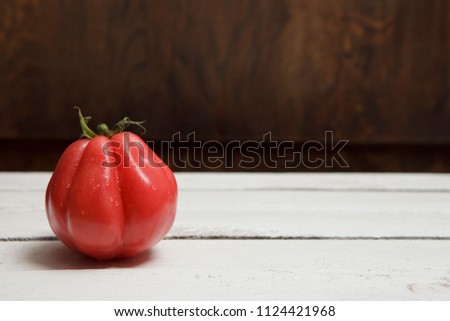 Buffallo heart tomato on left side of wooden garden table, fresh with drops of water