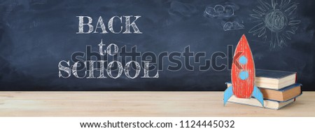 Back to school banner. Painted cardboard rocket next to books in front of classroom blackboard
