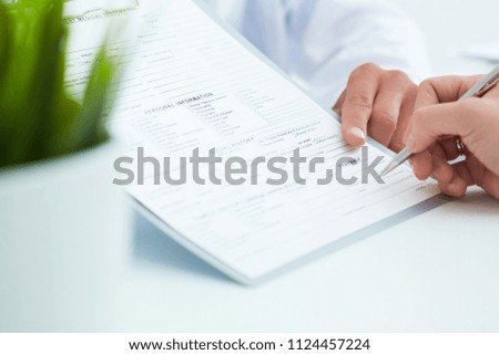 Female patient signs the medical form at doctors office with the help of a doctors assistant. Just hands over the table.
