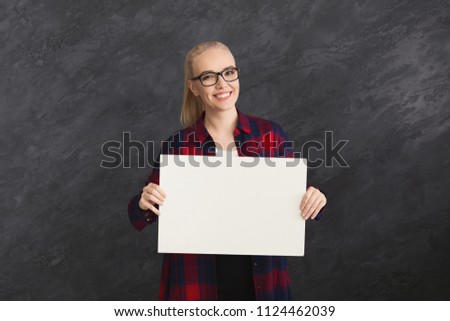 Young woman holding blank white banner with copy space, on gray background