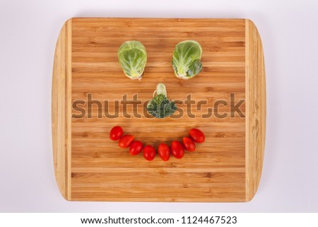 Happy Vegetables smiley face Brussel sprouts broccoli and cherry tomatoes on a bamboo light wood cutting board  