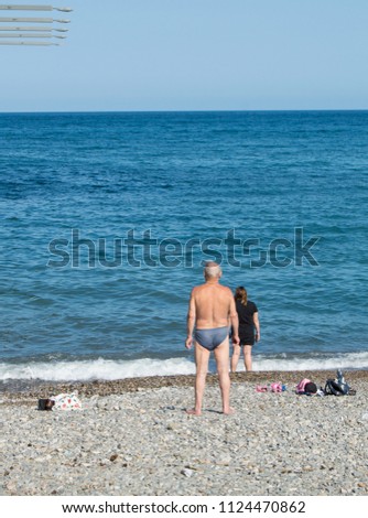 An elderly gray-haired man standing on the beach and preparing to swim in the cold sea, the concept of hardening and healthy lifestyle