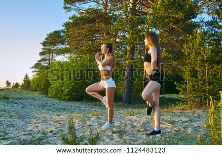 Two girls meditating practicing yoga fitness exercise at sunset  on the beach with a pine forest in the background