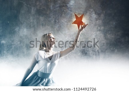 Young attractive woman reaching for the star. Take a star from the sky, dreams and plans, concept. Textured gray background