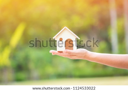 The buying a new real estate as a gift to family or the one loved concept, a woman hand holding a home model in the public park.