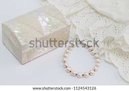 Pearl bracelet, mother of pearl, trinket box and white lace on white background