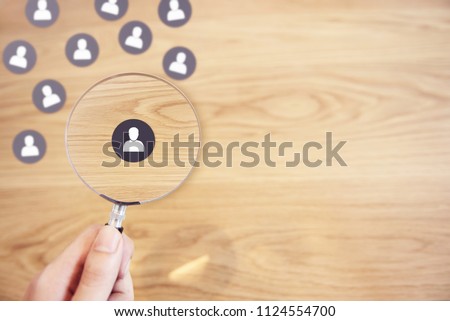 Human resources management and recruitment concept, Hand holding magnifying glass search people paper icon on top desk.
