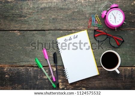 To do list in notepad with cup of coffee, glasses and pink alarm clock on grey wooden table