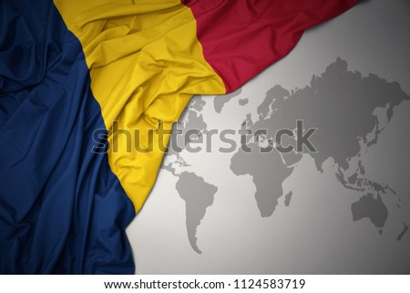 waving colorful national flag of chad on a gray world map background.