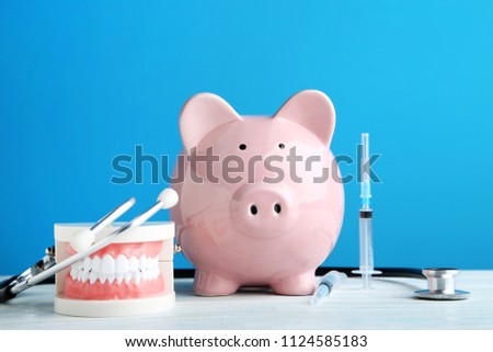 Pink piggy bank with stethoscope, syringe and teeth model on blue background