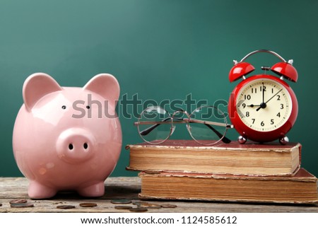 Pink piggy bank with glasses, books and alarm clock on wooden table