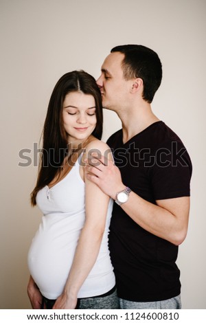 Image of husband standing and holding belly of pregnant wife hands. Woman, girl and loving handsome man kissing and hugging tummy at home. Loving Couple. Parenthood concept. Baby Shower. Family photo.