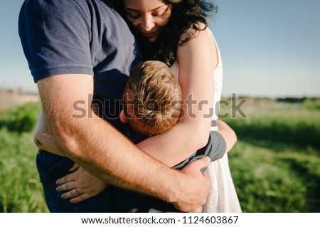The son hugging parents on nature. Mom, dad and boy walk in the grass. Happy young family spending time together, outside, on vacation, outdoors. The concept of family holiday. Royalty-Free Stock Photo #1124603867