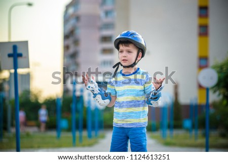 Little boy riding on rollers in the summer in the Park. Sad child in helmet learning to skate. Safety in sport.