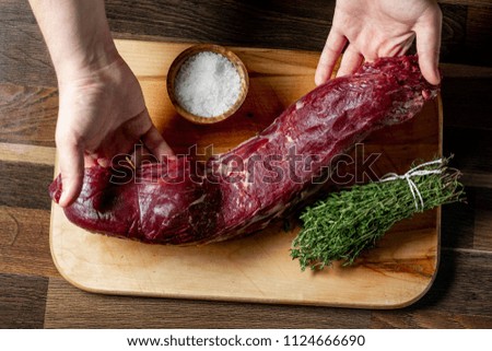 Cooking beef steak recipe - raw beef fillet in chef hands on cooking wooden table with herbs, salt and spices.