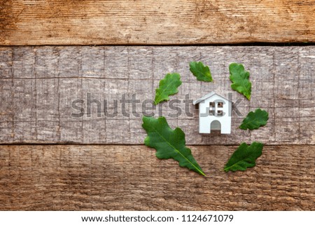 Miniature white toy model house with green oak leaves on wooden backgdrop. Eco Village, abstract environmental background. Real estate mortgage property insurance dream home ecology concept