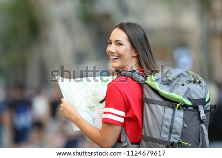 Happy teen tourist holding a paper guide and looking at camera on the street
