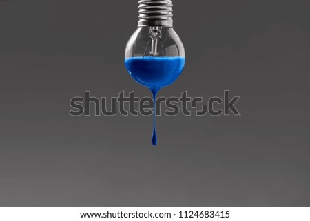Glow-lamp with blue paint on the gray background in the studio. Paint is dripping down from it. Closeup. Horizontal.