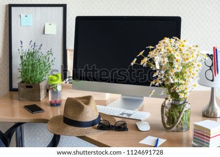 Workspace with computer, same office supplies,  flowers, infused water bottle, hat and glasses on a wooden desk