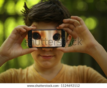teenager boy make funny picture with cats eyes on cell phone outdoor summer photo