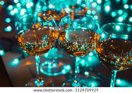 Glass glasses with wine on the background of luminous garlands. Good New Year spirit. Multicolored bokeh.