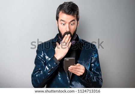 Handsome man with sequin jacket talking to mobile on grey background
