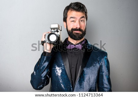 Handsome man with sequin jacket filming on grey background