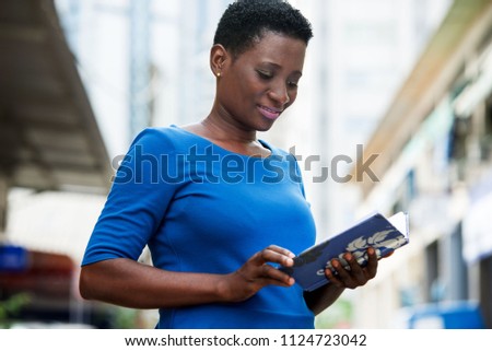 young girl standing in blue camisole reading with a smile.