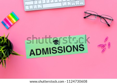 College admission concept. Word admissions with graduation cap sign on pink student desk with computer top view copy space