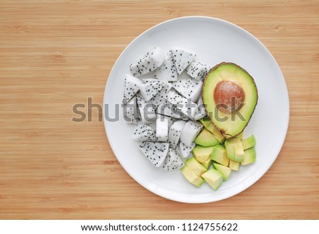 Fresh sliced fruit (avocado and dragon fruit) on white plate against wooden board background with copy space.