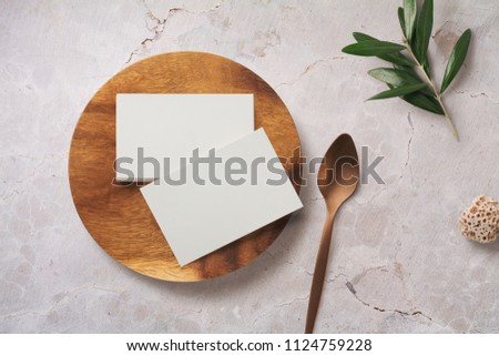 styled minimalist food or restaurant related branding mock-up with stack of business cards on a wooden plate and olive twig on a blush marble background - top view / flat lay
