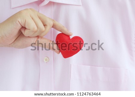 Businessman pulling out or into a red heart from the pocket of pink shirt