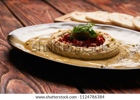 Hummus National Israeli cuisine. Hummus with harissa sauce and pistachios, close-up. Vegetarian diet food with pita bread on wooden cutting board.