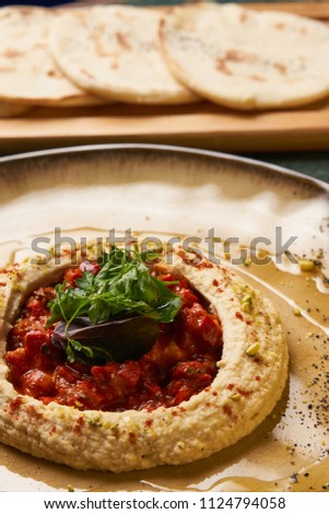 Delicious Hummus with harissa sauce and pistachios, close-up. Vegetarian diet food with pita bread on wooden cutting board
