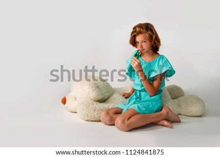 A young red-haired girl with freckles and a rose. Nearby a teddy bear. Shooting in the studio on a white background