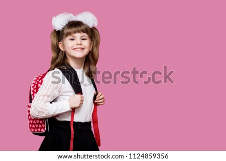 Cute smiling little girl in school uniform and white bows with backpack on pink background. Back to school. Education and school concept Royalty-Free Stock Photo #1124859356