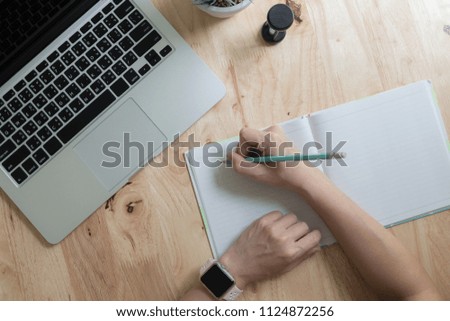 Woman studying with laptop and taking notes on a desktop at cafe. Top view