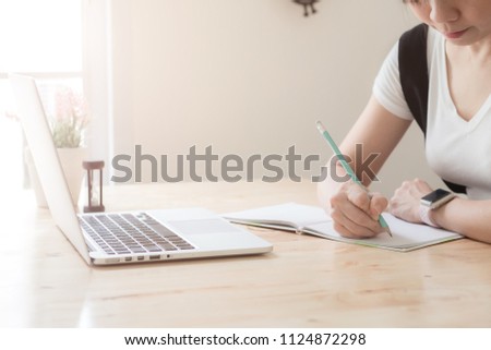 Woman studying with laptop and taking notes on a desktop at cafe