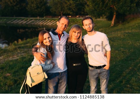 happy family hugged on the shore of the evening lake. An adult daughter and son embraces their mature parents