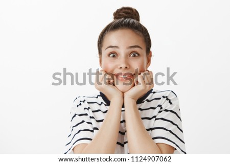 Woman excted to listen amazing stories. Good-looking impressed feminine girl with bun hairstyle, holding hands on chin and smiling broadly, waiting to hear interesting news over white wall Royalty-Free Stock Photo #1124907062
